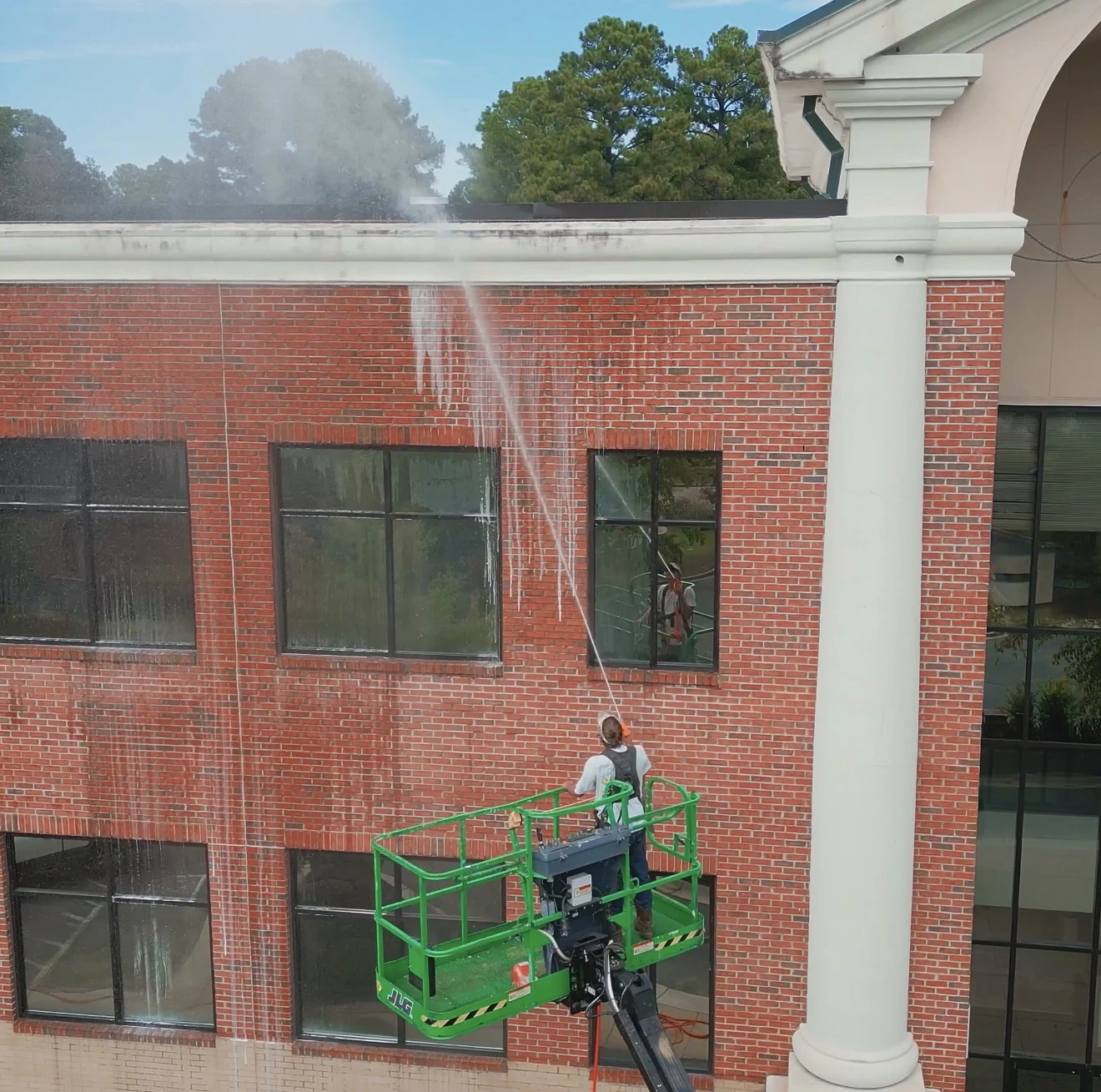 Exterior cleaning in progress on a brick commercial building, with a worker using a lift to reach the upper facade.